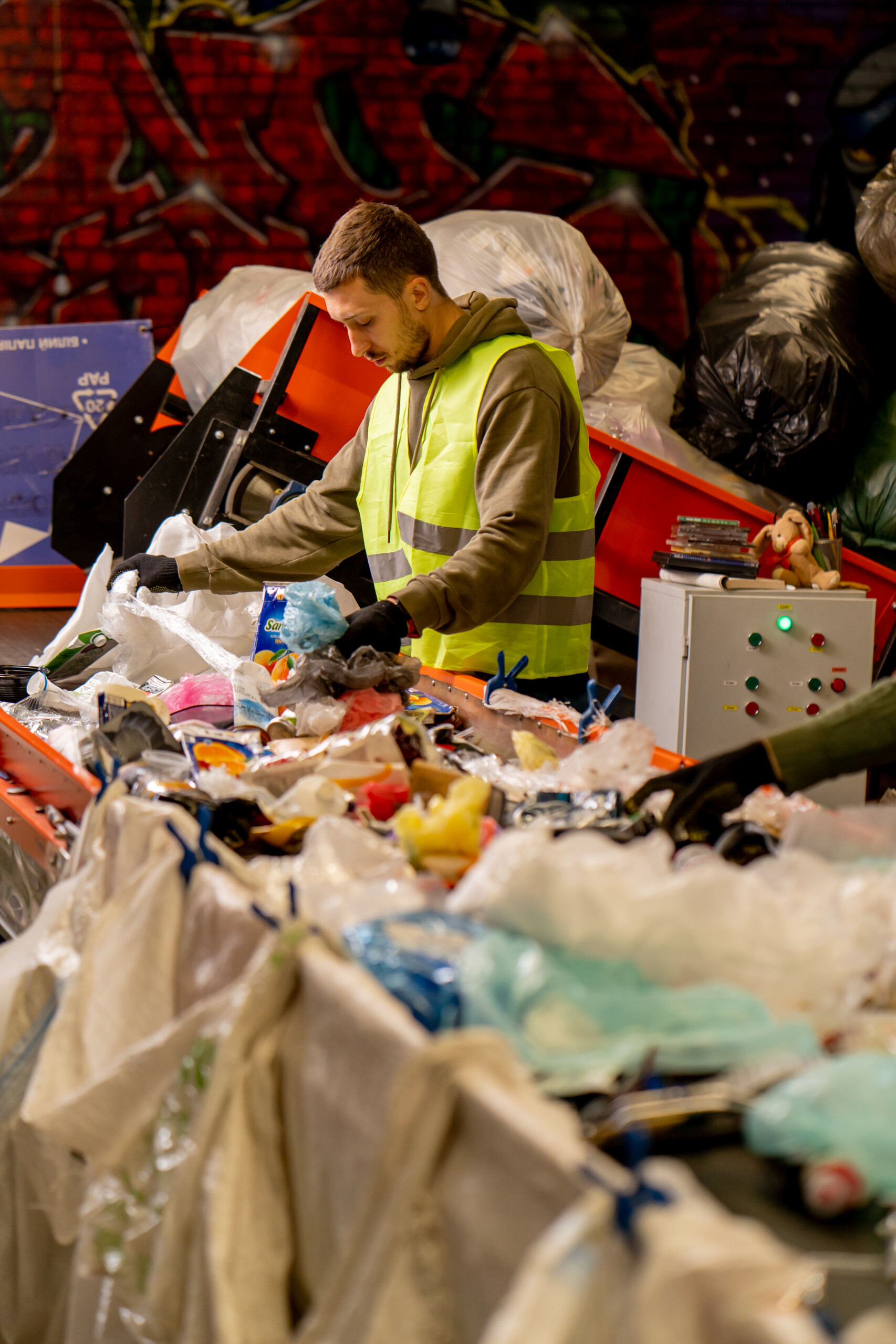 Side view of a sorter in gloves and a protective vest who sorts garbage on a special sorting line while working at a waste disposal station