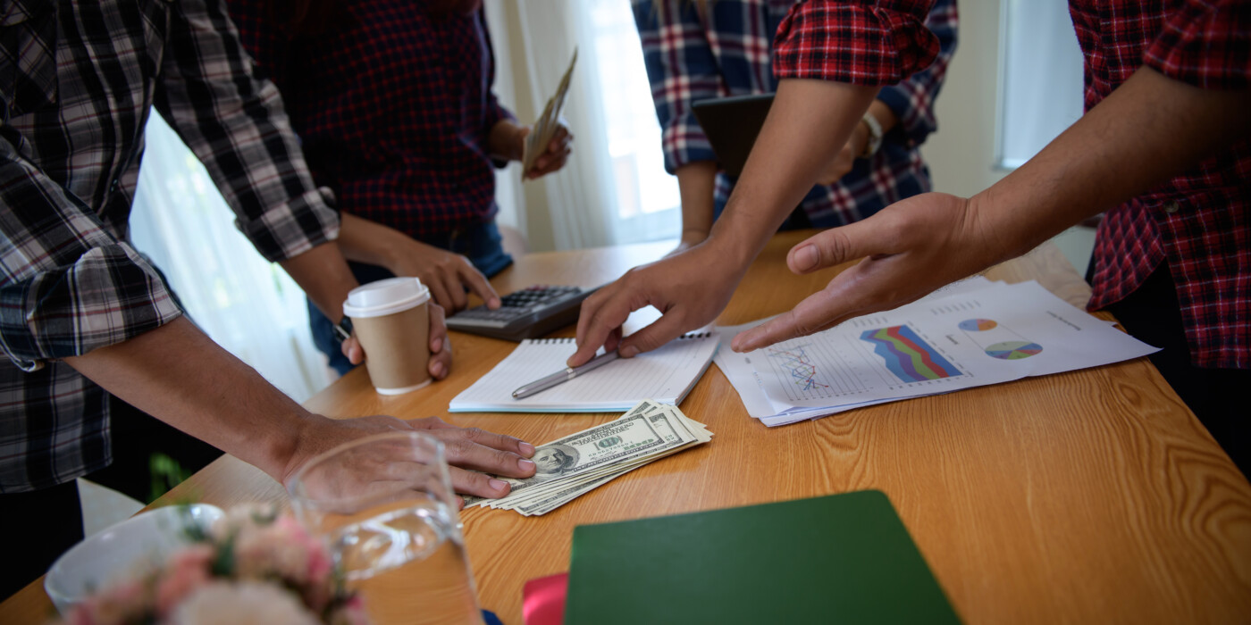 Jeunes hommes autour d'une table. Feuille de statistiques devant eux. billets en dollars.