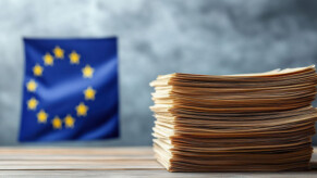 Drapeau européen en fond derrière une pile de documents.