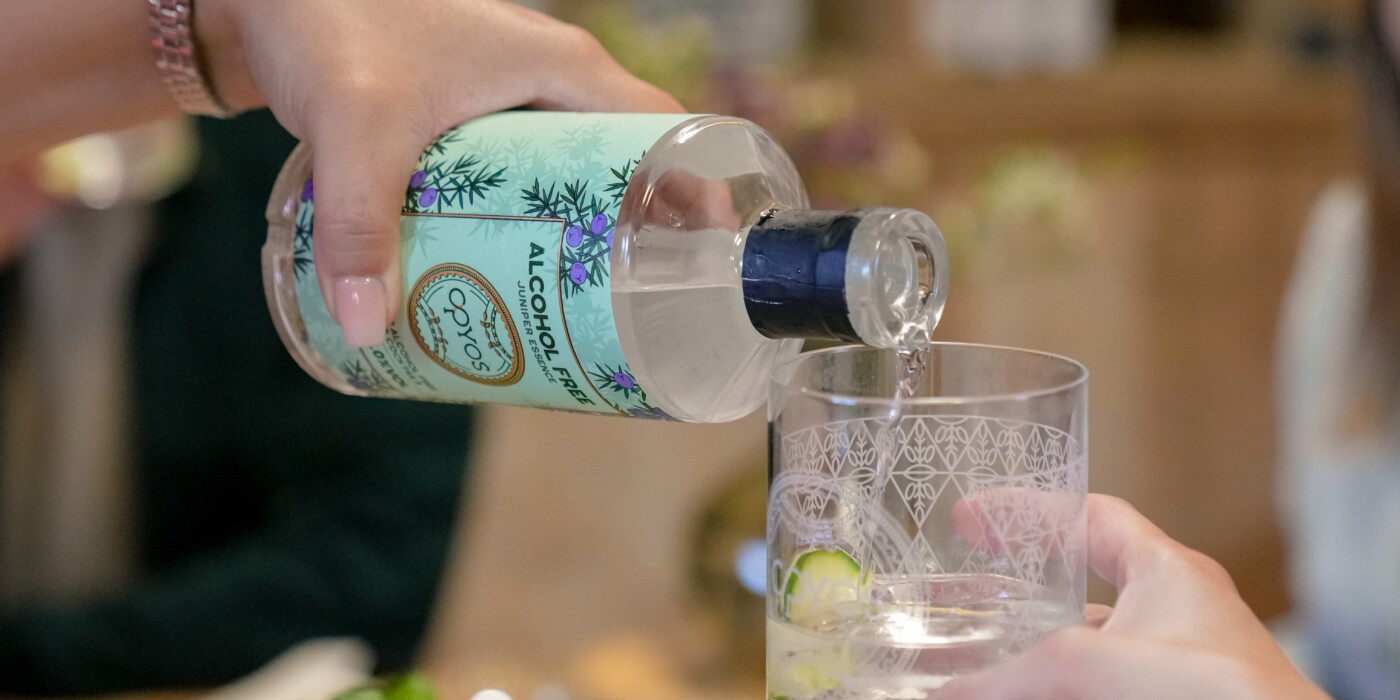 Une main servant un verre de gin Opyos sans alcool , lors d'un apértif.