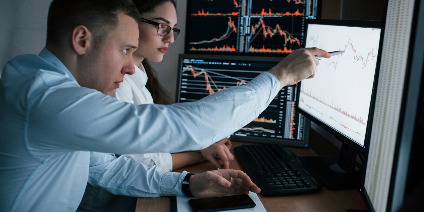 Deux traders suivent les cours de bourse sur des écrans d'ordinateurs