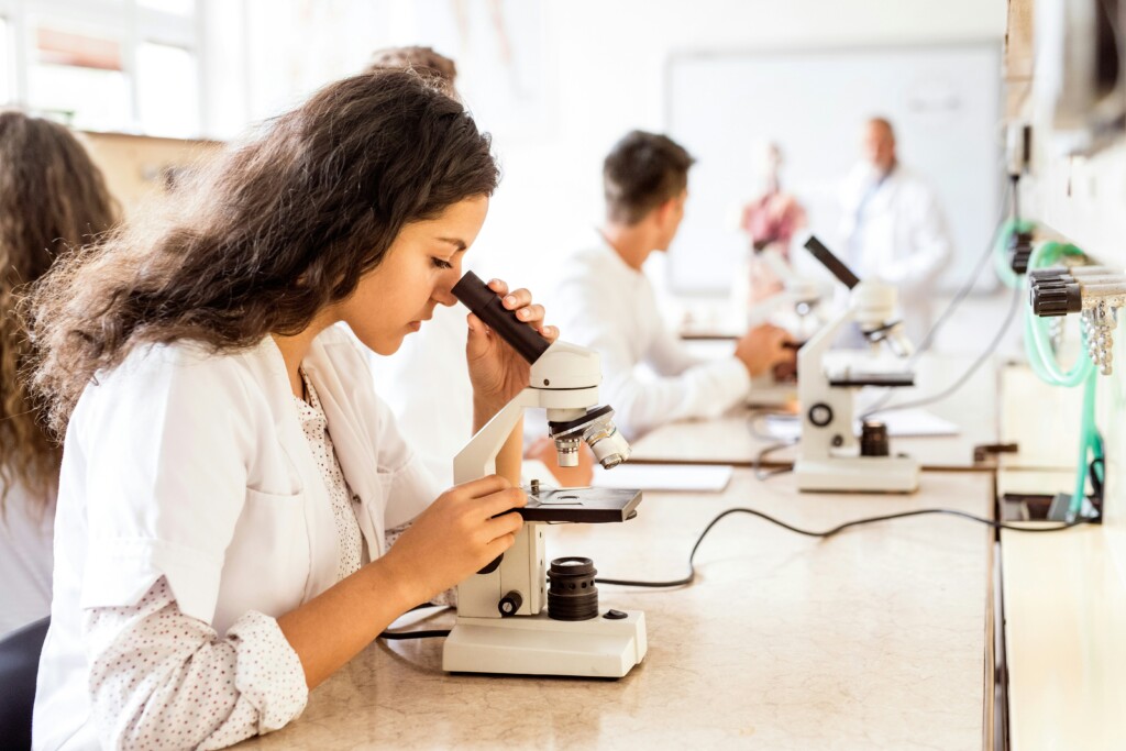 Jeune femme scientifique en blouse blanche, utilisant un microscope, dans un laboratoire.