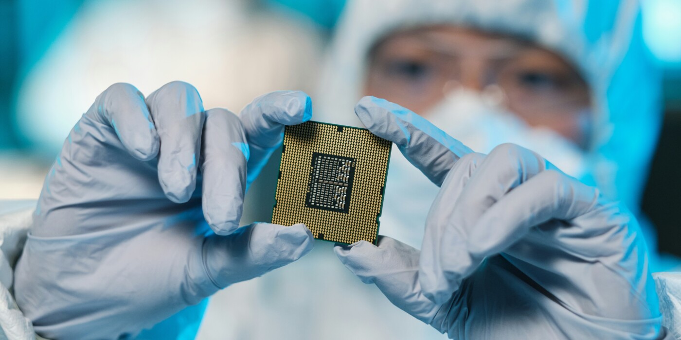 Un semi-conducteur dans les mains d'une personne gantée et cagoulée dans une salle blanche