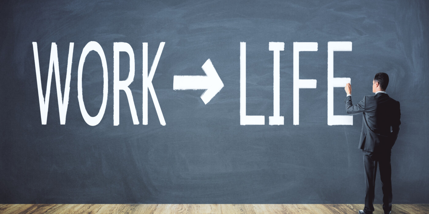 Un homme en costume devant un tableau où sont inscrits les mots work et life