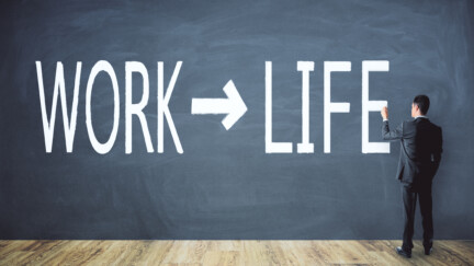 Un homme en costume devant un tableau où sont inscrits les mots work et life