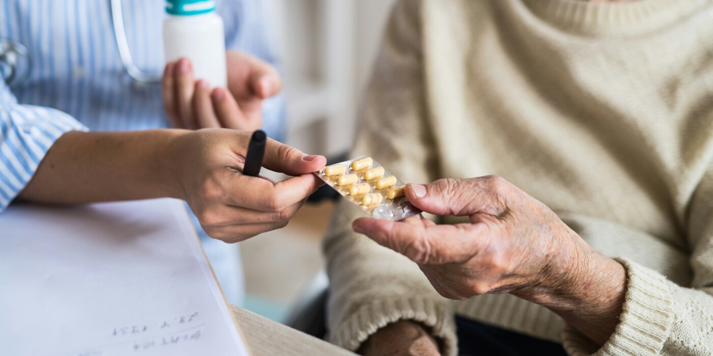 personnel soignant tendant une plaque de médicament à un patient âgé