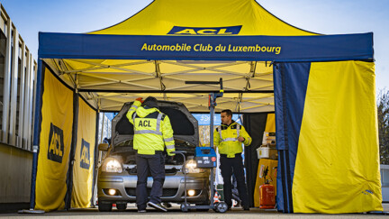 Campagne « Éclairage et pneus » 2026 : L’ACL et la SNCT reprennent la route 2 hommes sous une grande tente occupés à regarder sous le capot d'une voiture